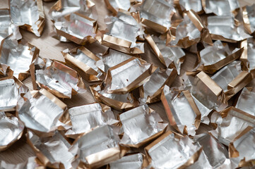 Pile of empty silver-gold candy wrappers. Top view. 