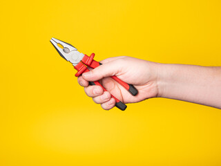 A hand holds a pair of pliers. Yellow background, no face, concept.