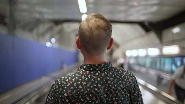 Man rides escalator down into London Underground station while crowds go by