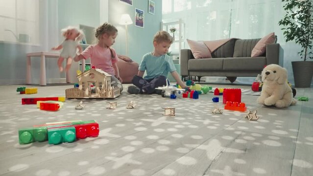 Siblings play with baby doll and robot dinosaur in nursery. Brother and sister sit on floor enjoying toys view through clearance in construction of cubes