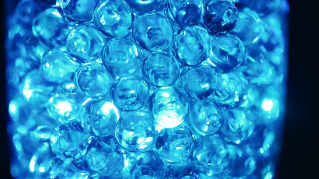 Water colored, blue gel balls. Super macro bubbles slow motion. Background with hydrogel balls with glitter. The concept of cosmetology. Luminous, shiny capsules.