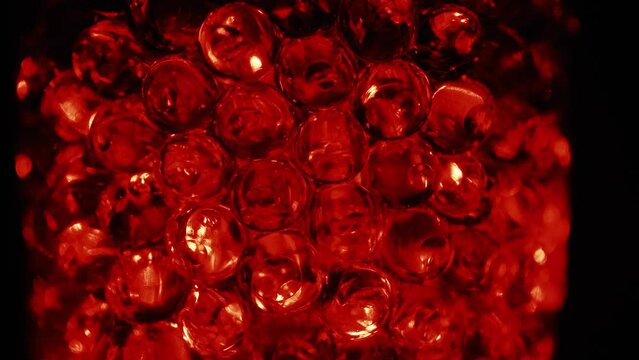Water colored, red gel balls. Super macro bubbles slow motion. Background with hydrogel balls with glitter. The concept of cosmetology. Luminous, shiny capsules of vitamins for the face under a