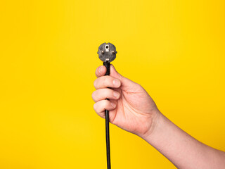 A hand holds a plug to which a black cable is attached.  No face, yellow background.
