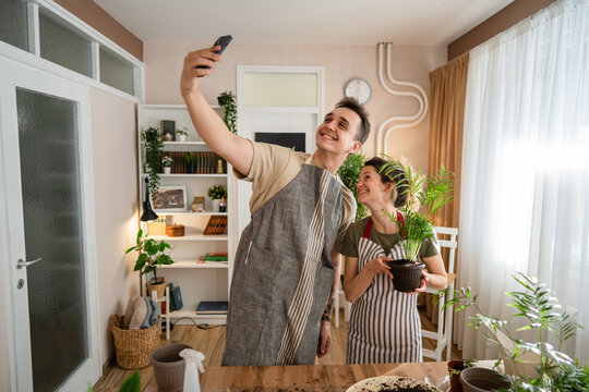 Couple caucasian man and woman wife and husband planting flowers together taking care of home plants real people domestic life family gardening concept take selfie photo with smartphone copy space