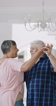 Vertical video of diverse senior couple having fun dancing at home, slow motion