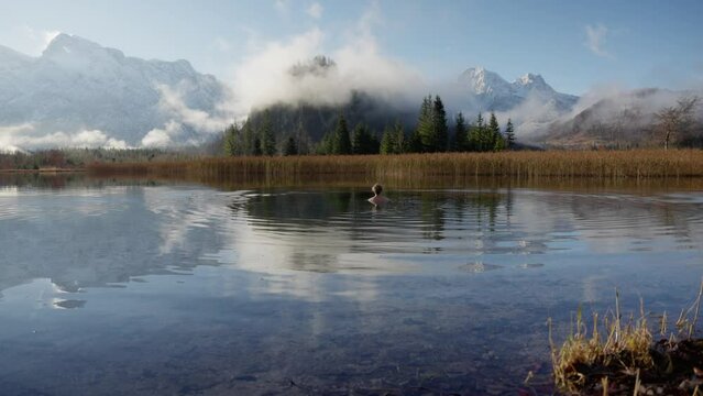 Blond man is doing an ice bath in a beautiful mountain lake in austria