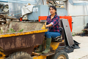 Female worker farmer working on tractor in orangery - obrazy, fototapety, plakaty