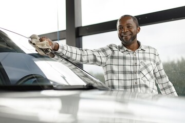Middle aged black man wiping his car with a rag outside in the car wash