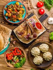 Rack of lamb, khinkali with meat, odjahuri with potatoes and pork, vegetable salad top view on old wooden table vertical