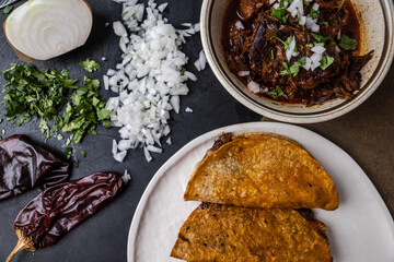 A plate of Mexican beef birria tacos witthe dipping sauce juices with shredded beef, herbs and broth