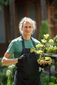 Young blonde man pruring bonsai at backyard garden