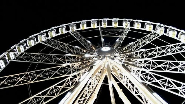 giant attraction illuminated with bright led light on dark black sky, large white metal ferris wheel with small cabin heap, modern entertainment diversity