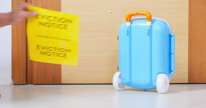 Hand removes judicial notice of eviction wooden door yellow sheet next to bright blue suitcase. Assistance restructuring debt relief training financial literacy, refinance loans. Legal advice broker
