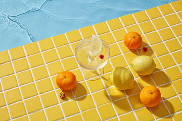 A glass with some lemons and oranges on the yellow mosaic background. A bird's-eye view