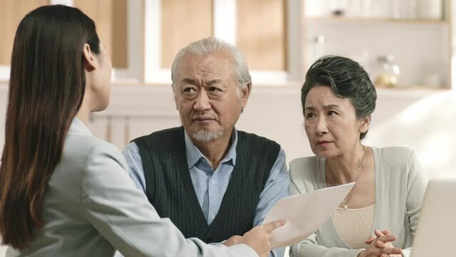 senior asian couple appears to be unconvinced and confused while listening to a saleswoman	