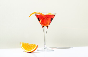 Martinez alcoholic cocktail drink with red vermouth, liqueur, orange bitter, zest and ice. Light beige background, hard light, shadow pattern. Minimalistic style - obrazy, fototapety, plakaty