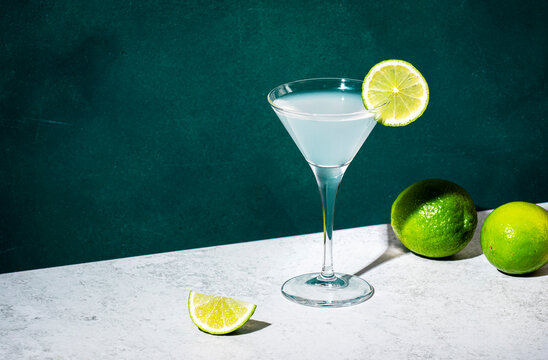 Vodka gimlet alcoholic cocktail drink with vodka, syrup, lime juice and ice, dark green background, bright hard light and shadow pattern