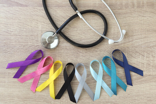 World cancer day background. Colorful ribbon arrange with stethoscope on the wooden table, cancer awareness. 