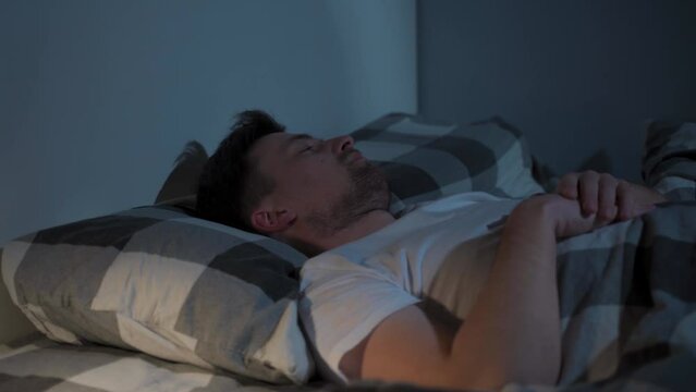 Young caucasian man spinning in bed, uncomfortable sleeping conditions. Nervous man cannot falling asleep at night, insomnia. Emotional and sleeping disorders concept. Male meeting dawn in bed.