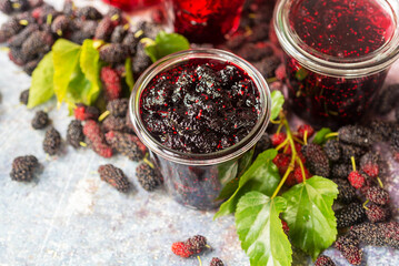 homemade mulberry jam in a glass jar with fresh mulberry with green leaves on rustic table...