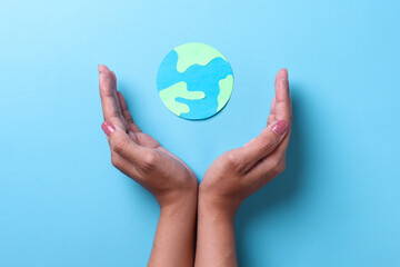 Top view of palms protect the globe made from paper isolated on blue background. World earth day concept. 