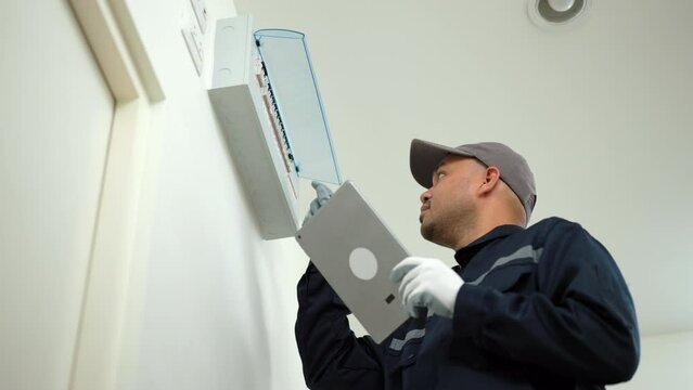 Electrician man in uniform using tablet for maintenance or fixing switches sockets  circuit breaker ,electrical system. Technician fixing an electric fuse at home. Home service concept.