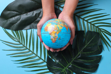 World Health Day, Save The Planet. Hands holding globes on various green leaf over blue background. 