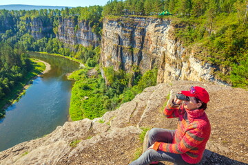 beautiful mature women sits on a high rock above the river and admires the big Aisian cliffs on a summer sunny day