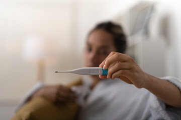 Young lady, checking her temperature on the thermometer she is holding in her hand.