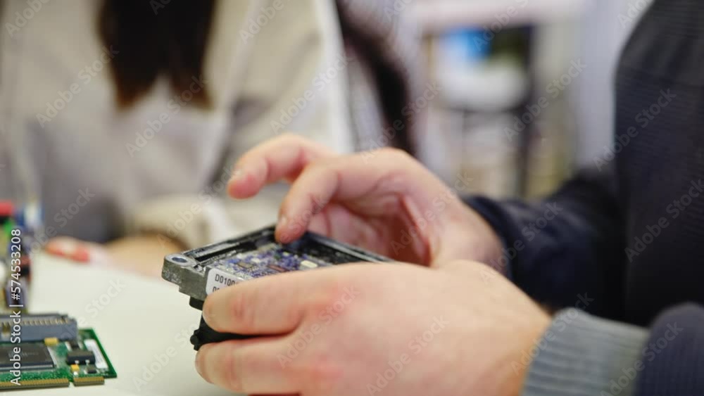 Poster closeup of a man showing something with his hands on a circuit board to a coworker..