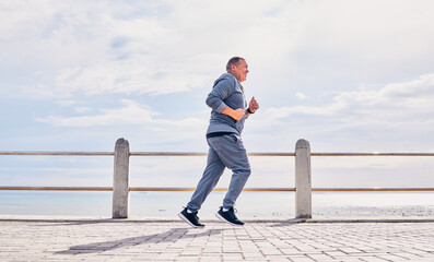 Senior man running outdoor at beach promenade, sky mockup and energy for body, wellness and cardio workout. Elderly male, exercise and runner at seaside for sports training, fitness or healthy action
