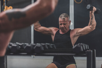 An old German man in his 60s doing a set of seated Y-raises at the gym. Limited range of motion due to age.
