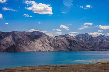 beautiful landscape of enormous mountain background compare to curve beach in front of the giant cystal clear blue lake in Pangong tso, Leh Ladakh, India