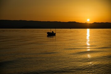 Sunset at the sea on a chain of hills, the entire sky shines in golden yellow colors, the sun is reflected in the water, on the sea a small boat.