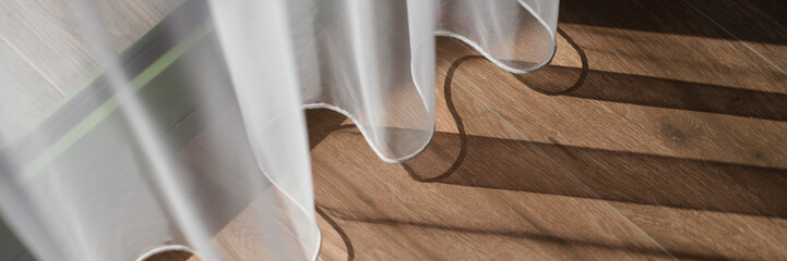 Closeup of light white curtains and brown wood laminate by window