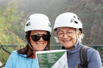 Senior women hikers with helmets standing on the top of mountain looking at map - Smiling climbing tourists enjoying holidays and healthy lifestyle - Freedom, success sport concept