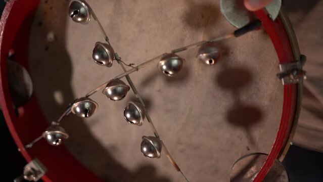 A red tambourine with a leather membrane with bells is shaken close-up, slow motion