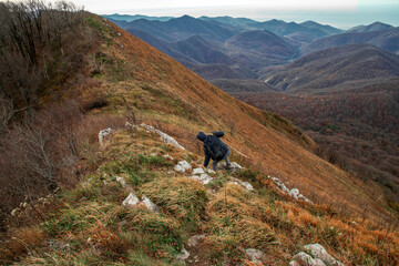 Fototapeta na wymiar A young man with a backpack descends from the top of the mountain. A young man on top of a mountain enjoying nature. A man going hiking in the Caucasus mountains. A tourist in the mountains. 