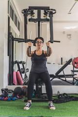 A short haired asian woman does a set of chest flys on a pec deck machine at the gym. Targeting the pectoralis muscles