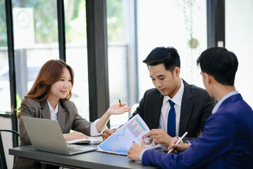 Group of young Asian business people discussing business plan at modern startup in creative business discussing work modern office building.