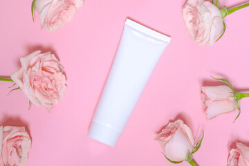 Obraz na płótnie Canvas White empty cosmetic tube, on a pink background with delicate pink roses. Natural cosmetics with rose extract or skin care spa salon or organic spa salon mockup