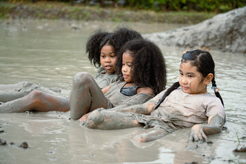 Group of happy children girl playing in wet mud puddle on summer day in rainy season