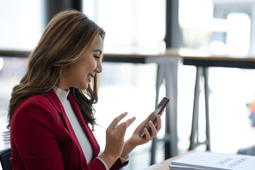 Beautiful asian businesswoman working with laptop computer is using mobile phone for talking. Finance business contacts in real estate projects in her office.
