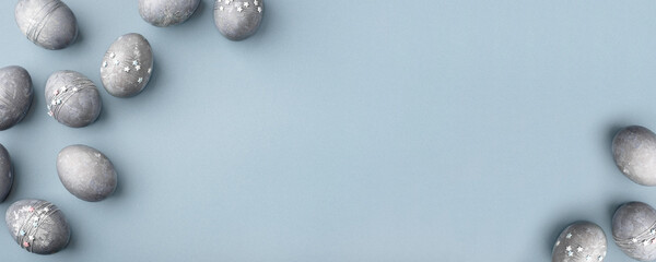 Festive Easter background. Gray-blue Easter eggs with stars on a blue table. Banner with a place for text. Top view.
