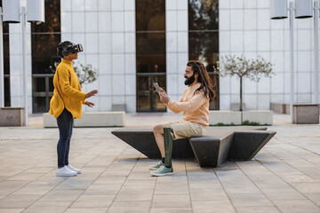 Young couple using VR glasses in the city center with headsets. Beautiful hispanic girl trying virtual reality 360 video and 3D video app man with prosthesis leg uses remote control