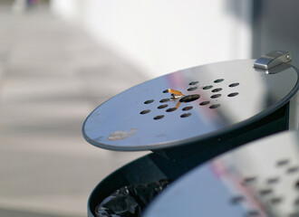 Close-up photo of a cigarette butt on a metal ashtray on top of a trash can with a blurry background
