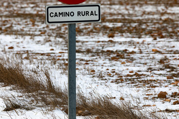 Señal de camino rural con un campo arado y nevado de fondo