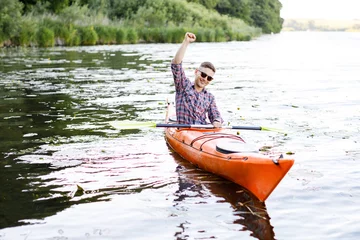 Foto op Canvas Adult caucasian man is sitting in a kayak and greetings. The concept of the water activities. © nazariykarkhut