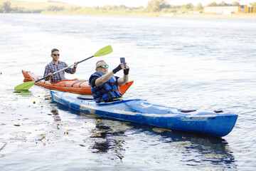 Two young men sit in kayaks and take a selfie with a portable camera. The concept of water entertainment.
