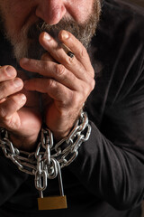 man with a cigarette in his mouth and his hands in chains,addiction concept